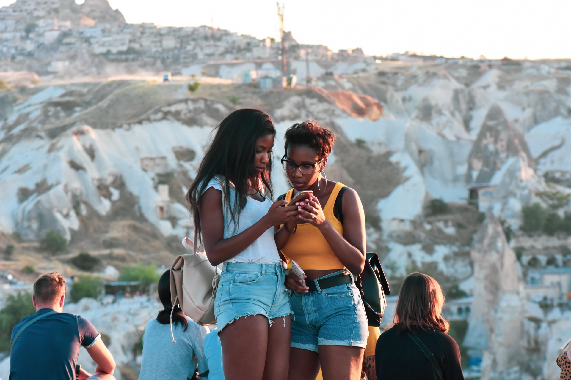 Two friends on a hilltop looking at a phone together, with other visitors around them.