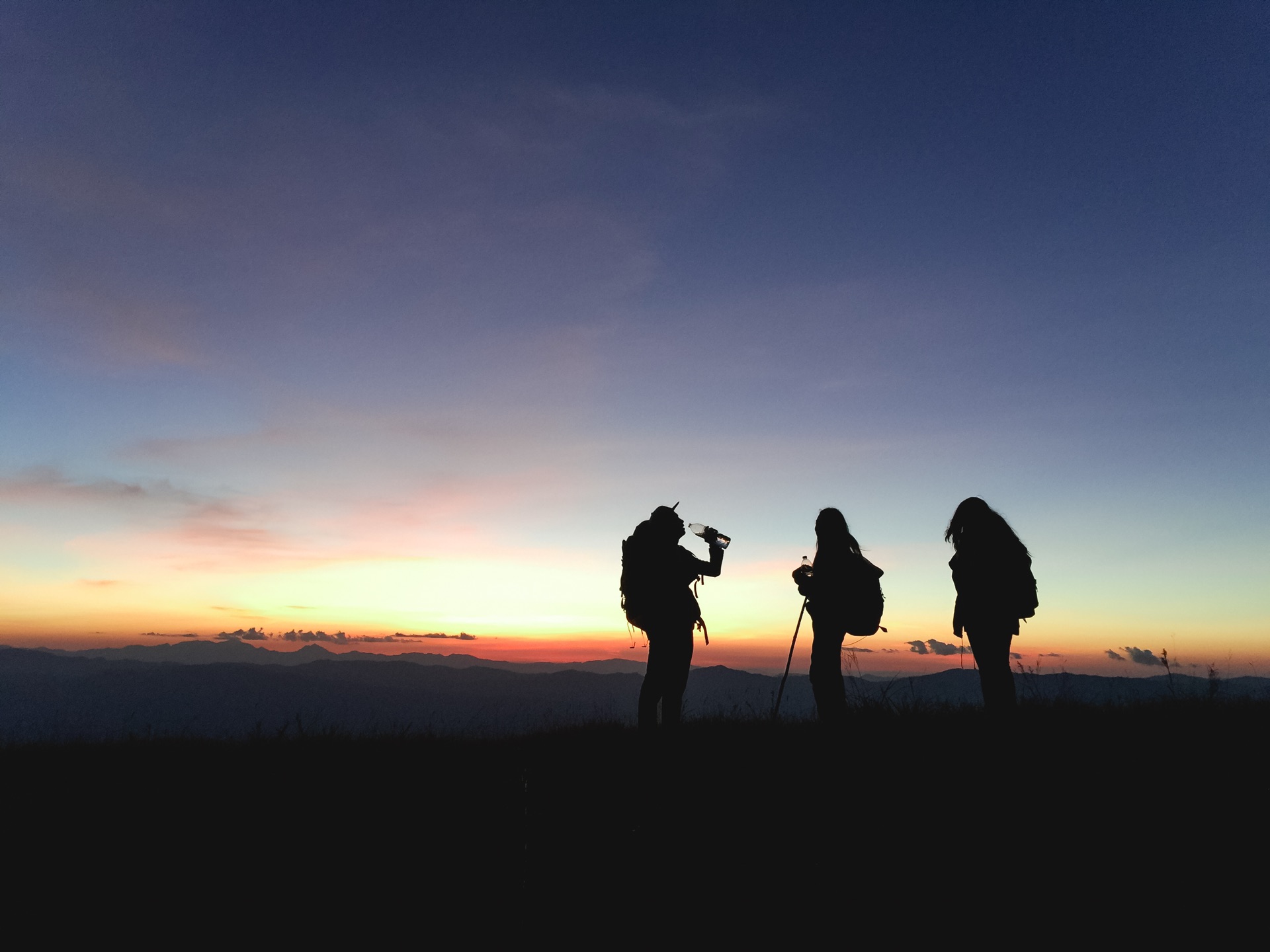 Three hikers with backpacks, silhouetted on a ridge at sunset.