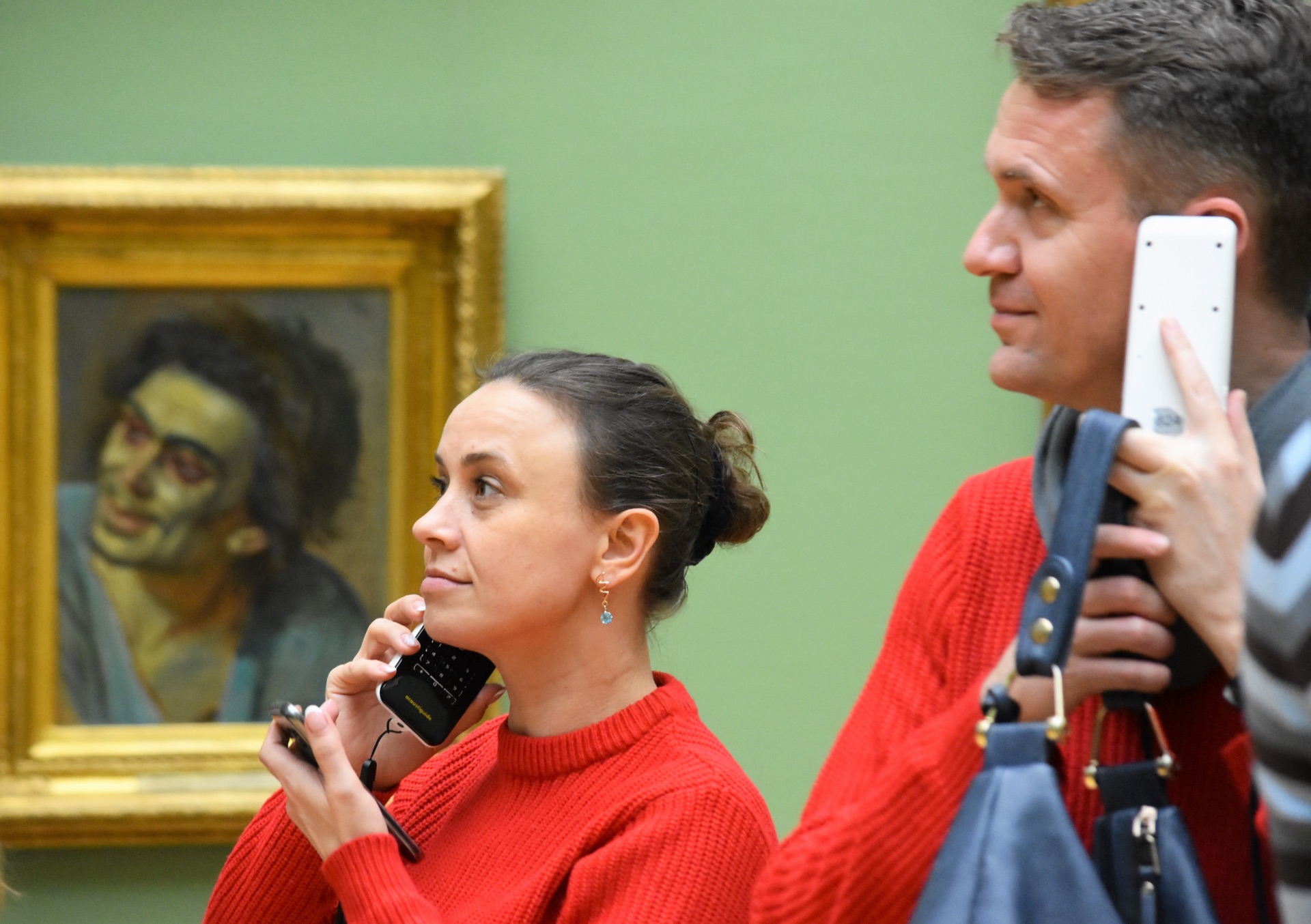 A man and a woman in a gallery, listening to audio guides in front of a portrait.