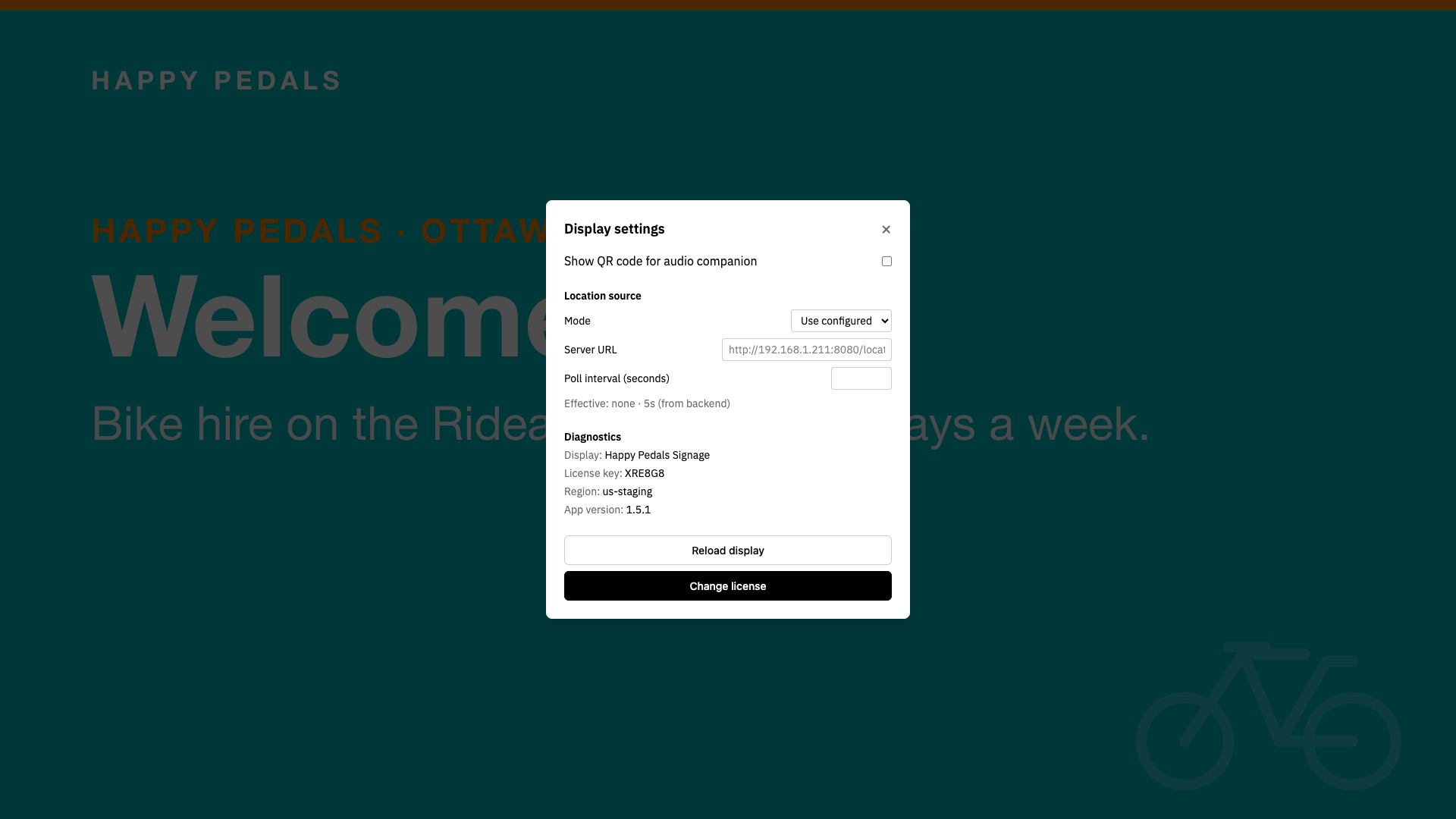 The Display settings overlay on the Happy Pedals shop counter, showing the audio companion checkbox, location source, Diagnostics with project, key, region and app version, and Reload display.