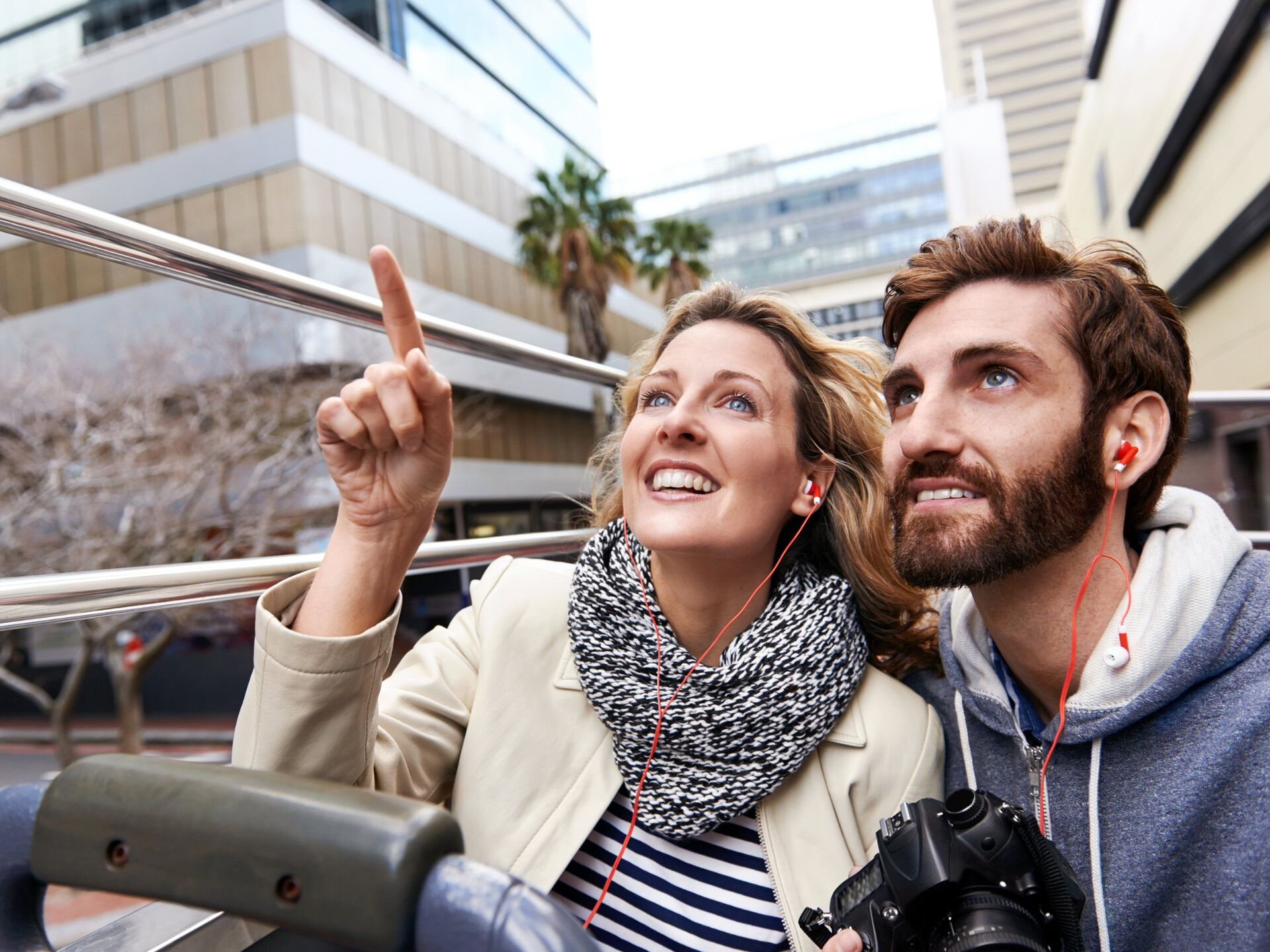 Two visitors on the top deck of a sightseeing bus, one pointing at something they've spotted.
